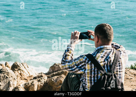Ein erwachsener unkenntlich männlichen Backpacker Fotos auf ein Mobiltelefon, um einen schönen Blick auf den Atlantik vom Ufer aus. Stockfoto