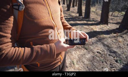 Thema Tourismus und Technologie. Jungen kaukasischen Mann mit Bart und Rucksack. Wandern touristische in einem Pinienwald verwendet die Technologie, Hand Handy Stockfoto