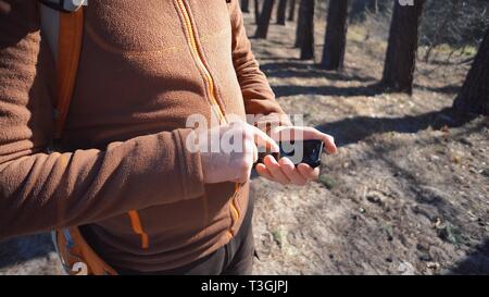 Thema Tourismus und Technologie. Jungen kaukasischen Mann mit Bart und Rucksack. Wandern touristische in einem Pinienwald verwendet die Technologie, Hand Handy Stockfoto