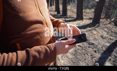 Thema Tourismus und Technologie. Jungen kaukasischen Mann mit Bart und Rucksack. Wandern touristische in einem Pinienwald verwendet die Technologie, Hand Handy Stockfoto