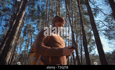 Thema Tourismus und Technologie. Jungen kaukasischen Mann mit Bart und Rucksack. Wandern touristische in einem Pinienwald verwendet die Technologie, Hand Handy Stockfoto