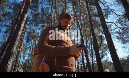 Thema Tourismus und Technologie. Jungen kaukasischen Mann mit Bart und Rucksack. Wandern touristische in einem Pinienwald verwendet die Technologie, Hand Handy Stockfoto
