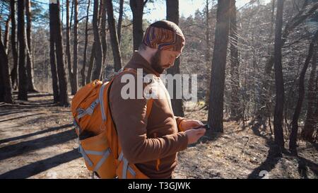 Thema Tourismus und Technologie. Jungen kaukasischen Mann mit Bart und Rucksack. Wandern touristische in einem Pinienwald verwendet die Technologie, Hand Handy Stockfoto