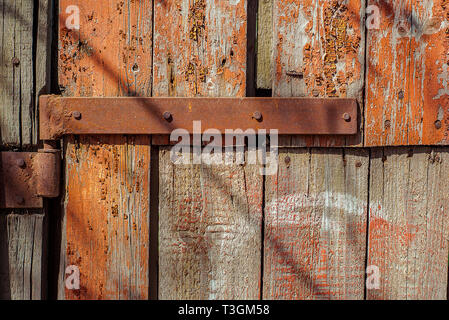 Rostige Tür Scharnier auf Holz Tür geknackt und zerkratzt, mit Resten der rote Lackierung. Horizontale grunge Textur. Stockfoto