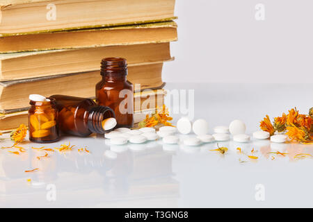 Medizin Kraut. Pflanzliche Pillen mit gesunden medizinischen Pflanzen. Getrocknete Blüten der Ringelblume, alternative Droge. Alte Bücher und Glasflaschen im Hintergrund. Stockfoto