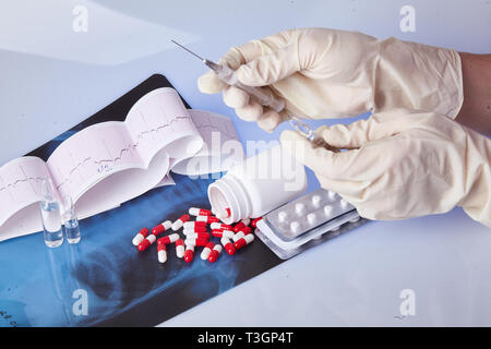 Zerstreut, Kapseln, Tabletten, Ampullen auf dem Tisch mit dem Elektrokardiogramm (EKG) und Röntgen. Hand in Hand mit einer Spritze mit Einspritzung. Healthcar Stockfoto