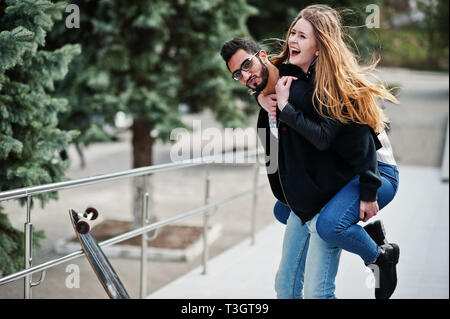 Cool gemischtrassiges Paar posiert mit Longboard. Europäische Mädchen sprang über die Schulter arabischen Mann. Stockfoto