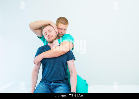 Männliche Patienten, die mit Massage Therapeuten. Ein chiropraktor stretching Hals seines Patienten in der Arztpraxis. Neurologische körperliche Untersuchung. Oste Stockfoto