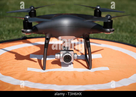 Vorderansicht eines schwarzen DJI Phantom 4 Pro Obsidian quadcopter Drohne auf einem orangefarbenen Landeplatz von Gras an einem sonnigen Tag umgeben Stockfoto
