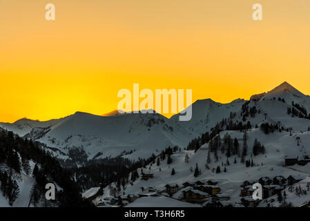 Orange Himmel und Sonnenstrahlen bei Sonnenuntergang über den Bergen in Obertauern, Österreich Stockfoto