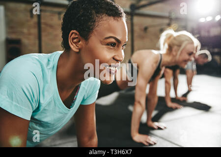 Passen junge afrikanische amerikanische Frau in Sportkleidung lächelnd, während sie Pushups während eines Trainings Klasse an der Turnhalle Stockfoto