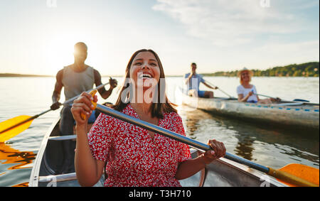 Junge Frau lacht beim Paddeln in einem Kanu mit ihrem Freund auf einem See mit ein paar anderen an einem sonnigen Nachmittag Stockfoto