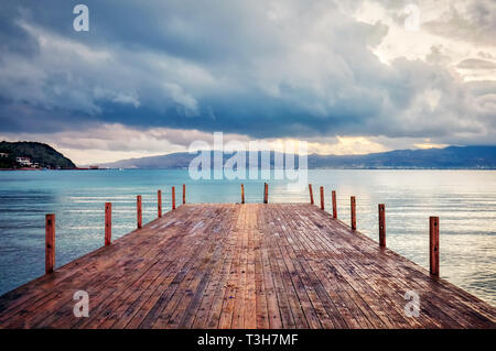 Holzsteg auf dem ruhigen Meer, Berge und bewölkter Himmel in der Morgendämmerung. Ruhiges Meer Landschaft. Stockfoto