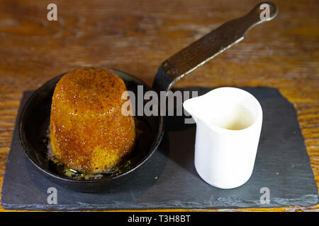 Sticky Toffee Pudding serviert mit Karamellsauce und ein Krug mit Vanillepudding. Das Dessert wird in der Pfanne serviert. Stockfoto