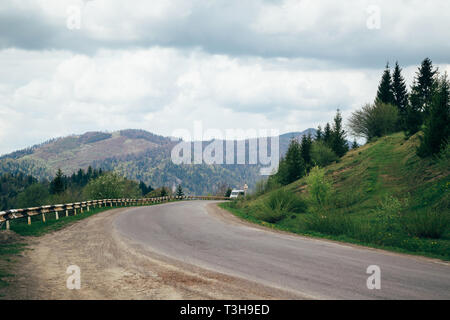 Alte asphaltierte Straße und ein Auto in die Berge mit bewölktem Himmel und Wald im Hintergrund Stockfoto