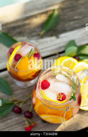 Hausgemachte erfrischendes Getränk. Wein Sangria oder Lochen mit Früchten in Gläsern, Cocktails mit frischem Obst, Beeren und Rosmarin auf einem hölzernen rustikalen Tisch. Stockfoto