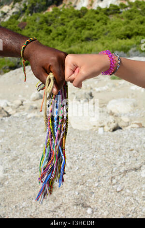 Hände von verschiedenen Rassen mit traditionellen afrikanischen Armbänder geschmückt, die Faust auf Faust Vereinbarung und Bündel von afrikanischen Armbänder vertikale Ausrichtung Stockfoto