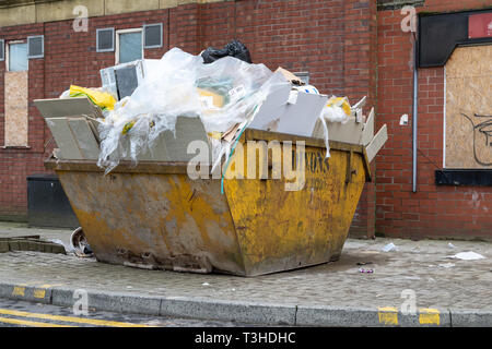 Eine gelbe Überspringen mit Müll auf einem Gehsteig in Bolton, Greater Manchester gefüllt Stockfoto