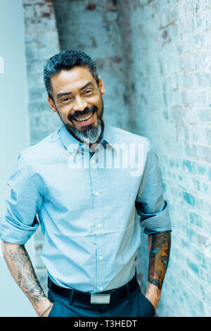 Porträt eines freundlichen, lächelnden Mann mit silber Bart, die Hände in den Taschen und Tattoos Stockfoto