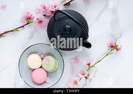 Teekanne und macarons mit Blumen auf Marmor Hintergrund. Ansicht von oben. Stockfoto