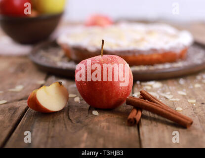 Apfelkuchen - frische Äpfel und zimtstangen vor einem hausgemachten Apfelkuchen auf einem rustikalen Holztisch Stockfoto