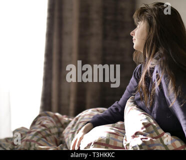 Cute brunette sitzt im Bett nach dem Aufwachen, schaut aus dem Fenster Stockfoto