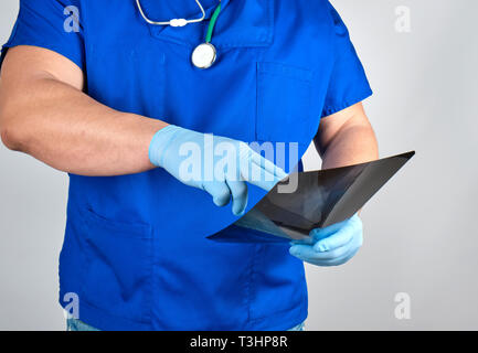 Arzt in der blauen Uniform und sterile Latex Handschuhe hält und untersucht, X-Ray, grauer Hintergrund Stockfoto