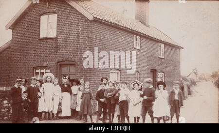 Vintage Edwardian photographische Postkarte zeigt eine große Gruppe von Jungen und Mädchen gemeinsam in einer britischen Dorf. Stockfoto