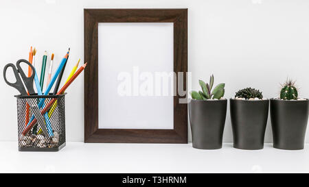 Leeren dunklen Bilderrahmen, Sukkulenten in Dunkle Töpfe und Buntstifte in der stand auf einem weißen Hintergrund. MockUp. Im skandinavischen Stil in das Innere. Stockfoto