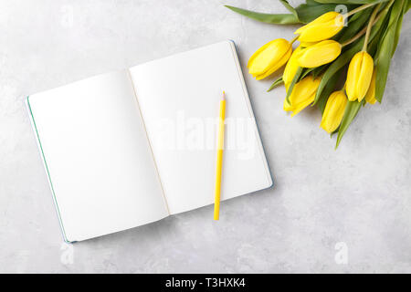 Leere Notepad und Strauß gelber Tulpen Blumen öffnen sich am grauen Stein table top Aussicht, flach. Weibliche desk top Stockfoto