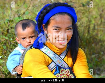 Junge Hani Frau (chinesische ethnische Minderheit) trägt ihr Baby auf dem Rücken in ein Baby sling mit ethnischen Design. Stockfoto
