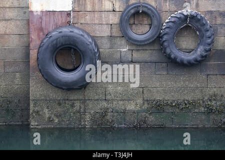 Autoreifen hängen am Seil gegen die Hafenmauer in Port dock Schiffe und Boote zu schützen. Stockfoto