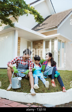 Familie und Kind sitzen auf einem Gras in ihrem Haus Garten nach Gartenarbeit Stockfoto