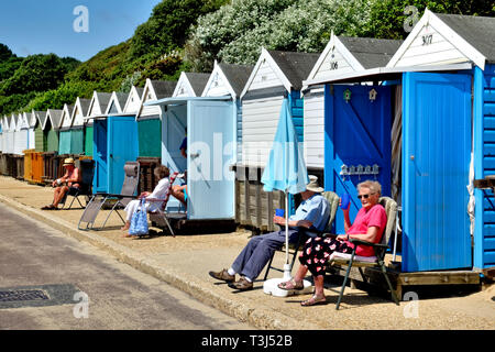 Menschen entspannen und die Sonne am Strand Hütten entlang West Spencer Court Promenade am Meer in Bournemouth, Dorset, England, Großbritannien genießen Stockfoto