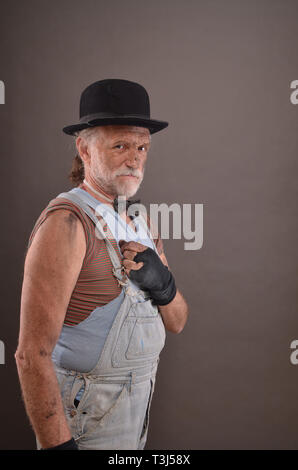 Alte, schmutzige Vagabond in verschlissenen Jeans und schwarzem Hut, aber stark und stolz, Studio shot Stockfoto