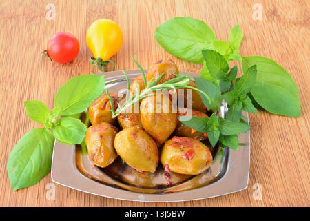 Würzige, warme grüne Oliven mit Frische, grüne aromatische Pflanzen und Cherry Tomaten in kleine, Metall Untertasse auf bambus holz- Tabelle Stockfoto