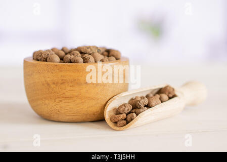 Menge ganze braune Ton Steine (leca) mit Houten und hölzerne Schaufel mit Blumen in einem weißen Küche Stockfoto