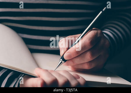 Linkshändige Frau schreiben Tagebuch, in der Nähe der Hände mit Bleistift und Notizbuch Stockfoto