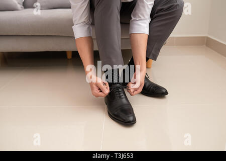 Der Mann die Hände binden Schuhbändern an seine neuen Schuhe. Menschen, Business, Fashion und Schuhe Konzept - Nahaufnahme der Mann Bein und die Hände binden Schnürsenkel. Stockfoto