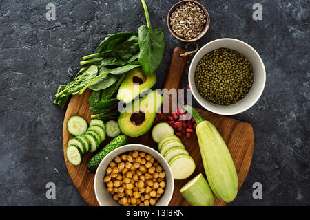 Zutaten zum Kochen vegetarische Kost, die Ansicht von oben. Rohes Gemüse und Getreide auf Holz Schneidebrett auf einem dunklen Hintergrund Stockfoto