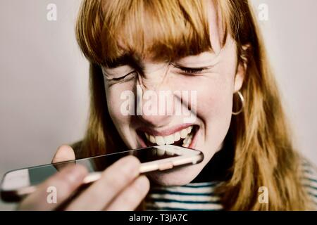 Mädchen, Teenager, rothaarige, beißen in Ihr aus Verzweiflung, Smartphone, studio Shot, Deutschland Stockfoto