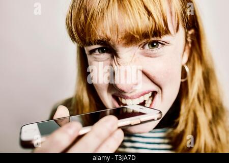 Mädchen, Teenager, rothaarige, beißen in Ihr aus Verzweiflung, Smartphone, studio Shot, Deutschland Stockfoto