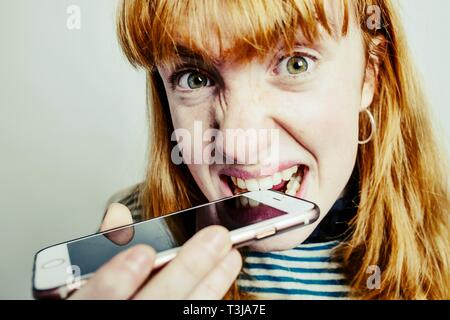 Mädchen, Teenager, rothaarige, beißen in Ihr aus Verzweiflung, Smartphone, studio Shot, Deutschland Stockfoto