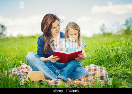 Mutter und Tochter lesen Buch über grüne Sommerwiese Stockfoto