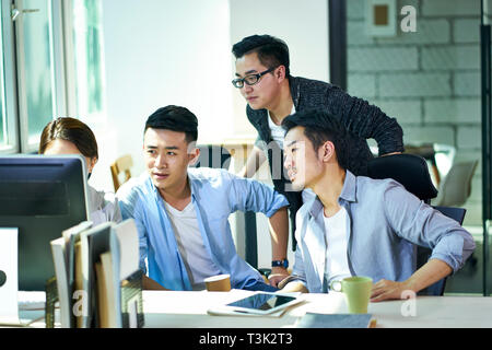 Vier jungen asiatischen Führungskräfte gemeinsam diskutieren business plan mit Desktop-PC im Büro. Stockfoto