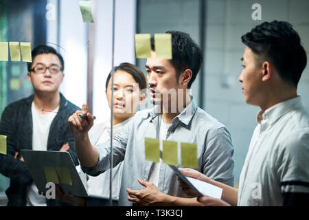 Junge asiatische Unternehmer von kleinen Unternehmen zeichnen Sie ein Diagramm auf Glas während der teamsitzung diskutieren und analysieren die Situation im Amt. Stockfoto