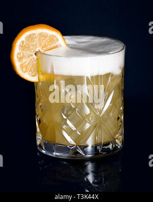 Einen Whiskey Sour Cocktail, serviert in einem altmodischen Glas mit einem orangefarbenen Rad garnieren auf schwarzem Hintergrund Stockfoto