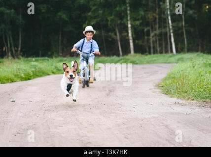 Kind Junge auf Fahrrad reiten, nachdem Hund läuft durch Land dirt road Stockfoto