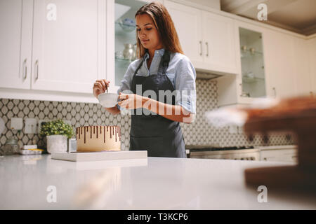 Frau Mischen flüssiger Schokolade in einer Schüssel, den Kuchen zu verzieren. Frau im Vorfeld vorbereiten Schokolade Kuchen zu Hause. Stockfoto