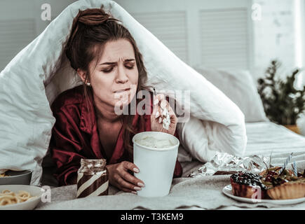 Betonte Frau mit einer Decke Süßigkeiten essen abgedeckt Stockfoto